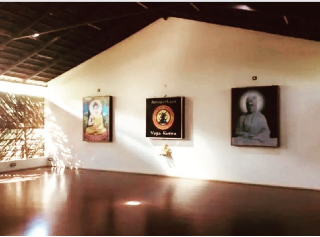 The same practice hall in the evening, lit from within: the timber roof in shadow, the three framed portraits along the white wall, and the red floor holding the light.