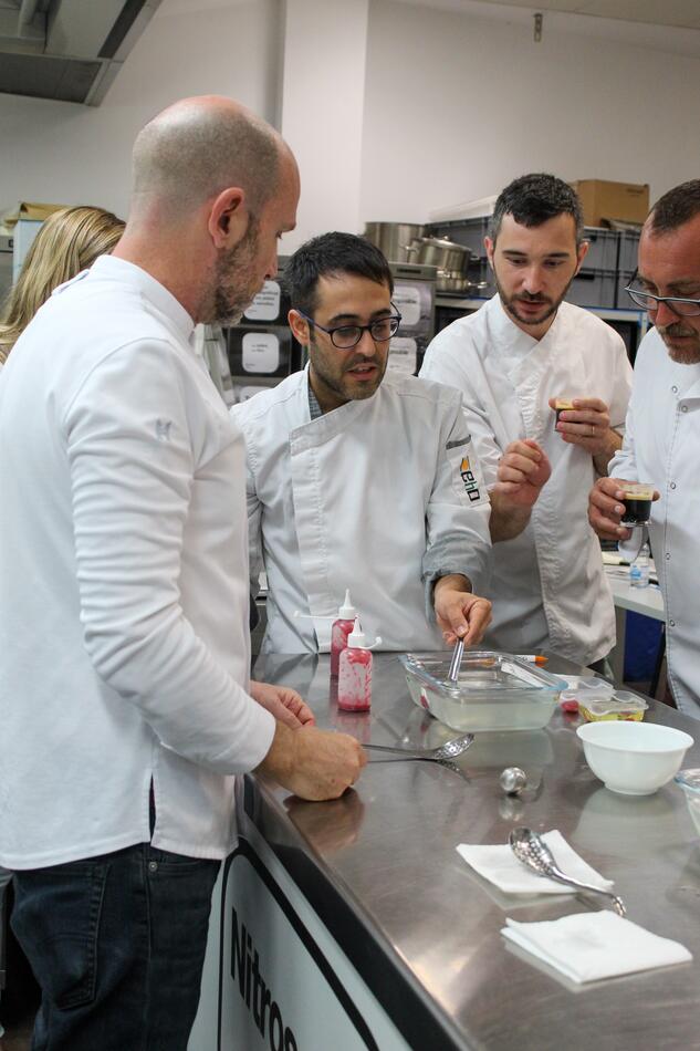 Cooks gathered around a spherification bath at the bench